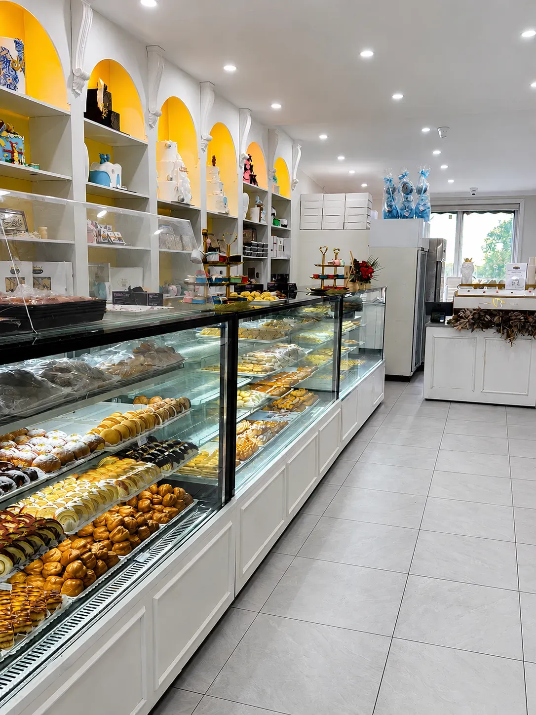 Inside Sweet Crown: glass counters of Persian pastries under gold-lit arched shelves